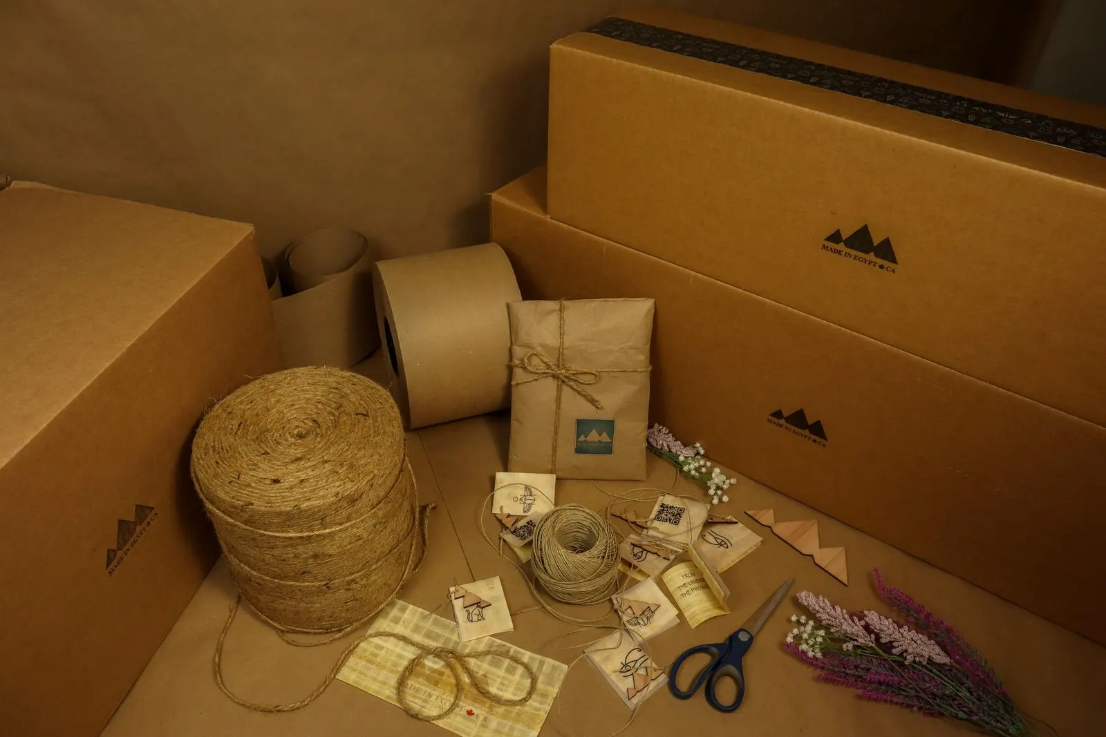 Kraft mailer boxes printed with a one-color black logo, next to kraft tape, twine and tissue-wrapped parcels